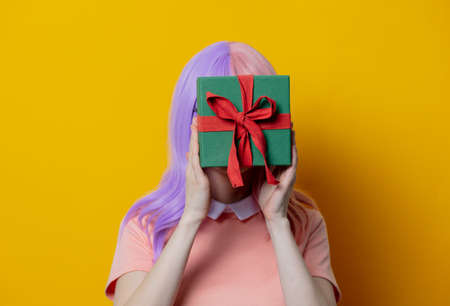 Girl with purple hair and pink dress hold gift box on yellow backgroundの写真素材