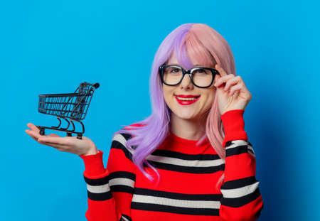 Girl with purple hair and red sweater hold black shopping cart on blue backgroundの写真素材