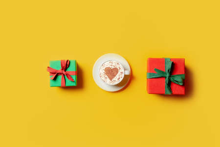 Holiday gifts and cup of coffee with heart shape on yellow background. Top viewの写真素材