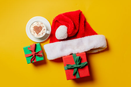 Holiday gifts, santa claus hat and cup of coffee with heart shape on yellow background. Top viewの写真素材