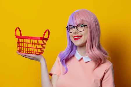 Girl with purple hair and pink dress with red shopping basket on yellow backgroundの写真素材