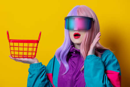 Style woman in VR glasses and 90s sport suit with shopping basket on yellow backgroundの写真素材