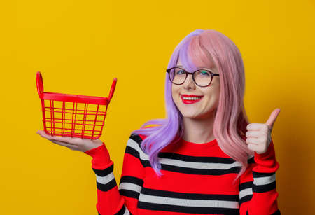Girl with purple hair and red sweater hold shopping basket on yellow backgroundの写真素材