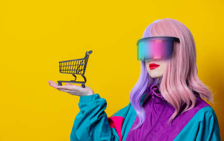 Style woman in VR glasses and 90s sport suit with shopping cart on yellow backgroundの写真素材