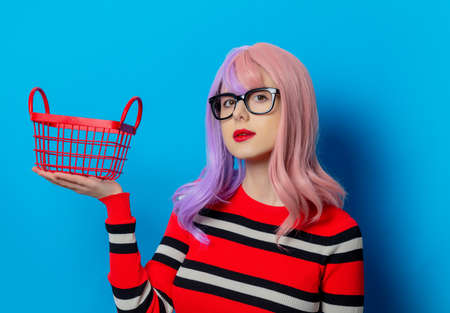 Girl with purple hair and red sweater with shopping basket on blue backgroundの写真素材