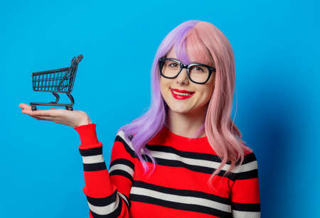 Girl with purple hair and red sweater hold black shopping cart on blue backgroundの写真素材