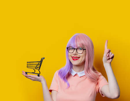 Girl with purple hair and pink dress with black shopping cart on yellow backgroundの写真素材