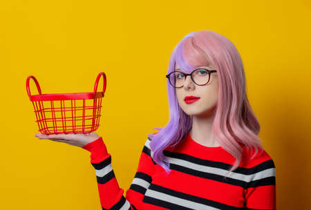 Girl with purple hair and red sweater hold shopping basket on yellow backgroundの写真素材