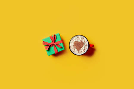 Holiday gift and cup of coffee with heart shape on yellow background. Top viewの写真素材