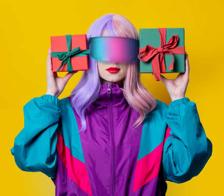 Style woman in VR glasses and 90s sport suit hold gift box on yellow backgroundの写真素材