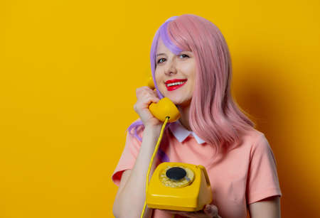 Girl with purple hair and pink dress hold dial phone on yellow backgroundの写真素材