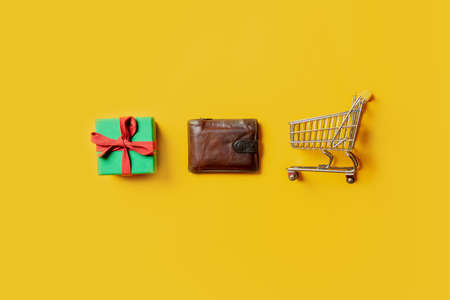 holiday gift box, wallet and supermarket cart on yellow background. Top viewの写真素材