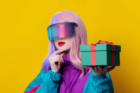 Style woman in VR glasses and 90s sport suit hold gift box on yellow backgroundの写真素材