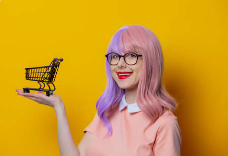 Girl with purple hair and pink dress with black shopping cart on yellow backgroundの写真素材