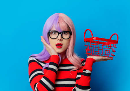 Girl with purple hair and red sweater with shopping basket on blue backgroundの写真素材