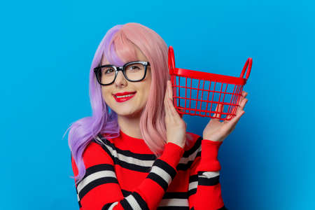 Girl with purple hair and red sweater hold black shopping cart on blue backgroundの写真素材