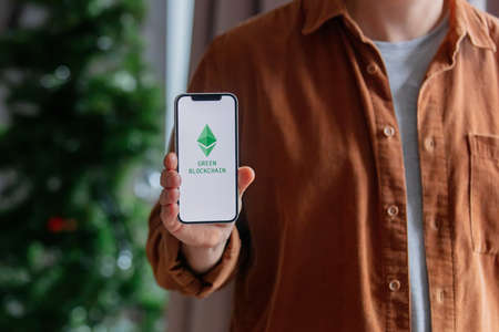 23 nov 2021 - Wroclaw, Poland: Man hold iPhone with green eco ethereum logo. Trend of 2022 yearのeditorial素材