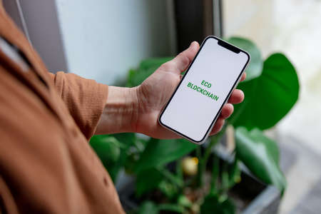 23 nov 2021 - Wroclaw, Poland: Man hold iPhone with green eco blockchain text. Trend of 2022 yearのeditorial素材