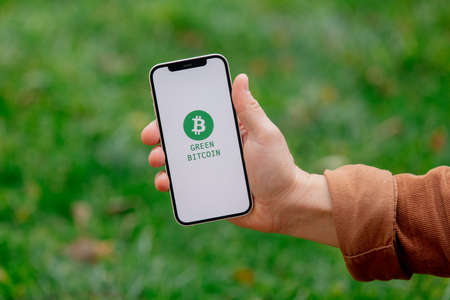23 nov 2021 - Wroclaw, Poland: Man hold iPhone with green eco bitcoin logo and blockchain text. Trend of 2022 yearのeditorial素材
