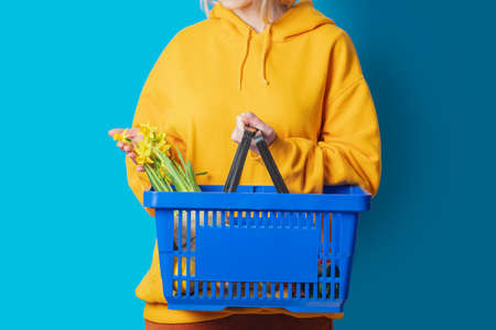 Stylish female in yellow hoodie with blue basket and flowers on blue backgroundの写真素材