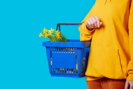 Stylish female in yellow hoodie with blue basket and flowers on blue backgroundの写真素材