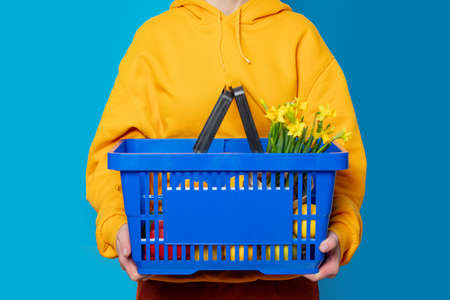 Stylish female in yellow hoodie with blue basket and flowers on blue backgroundの写真素材