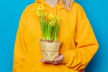 Stylish female in yellow hoodie with daffodil flowers on blue backgroundの写真素材