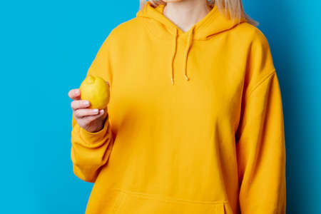 Stylish female in yellow hoodie with lemon on blue backgroundの写真素材