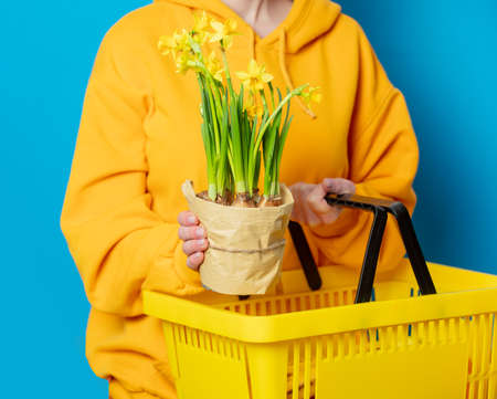 Stylish female in yellow hoodie with yellow basket and flowers on blue backgroundの写真素材