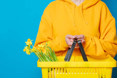 Stylish female in yellow hoodie with yellow basket and flowers on blue backgroundの写真素材