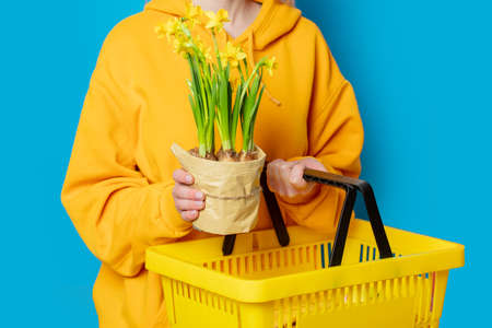 Stylish female in yellow hoodie with yellow basket and flowers on blue backgroundの写真素材