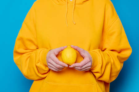 Stylish female in yellow hoodie with lemon on blue backgroundの写真素材
