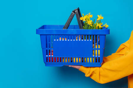 Stylish female in yellow hoodie with blue basket and flowers on blue backgroundの写真素材