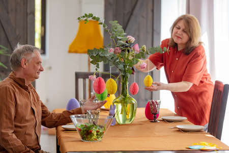 Grandparents decorate a bouquet of flowers at an Easter lunch sitting at the table at homeの写真素材