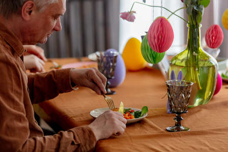 Grandpa eats at Easter dinner sitting at the table at homeの写真素材