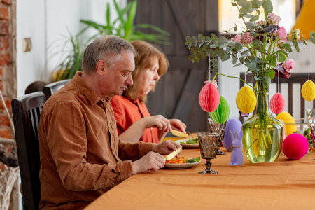 Grandpa and grandma eating at Easter dinner sitting at the table at homeの写真素材