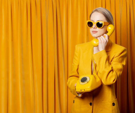 Stylish ukrainian woman in yellow sunglasses and jacket with dial phone on curtains backgroundの写真素材