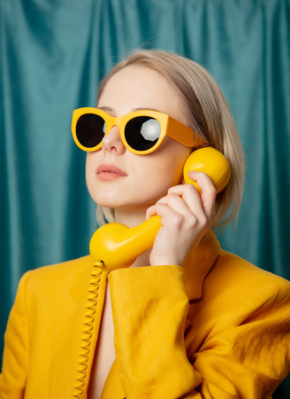 Stylish ukrainian woman in yellow sunglasses and jacket with deal phone on green curtains backgroundの写真素材