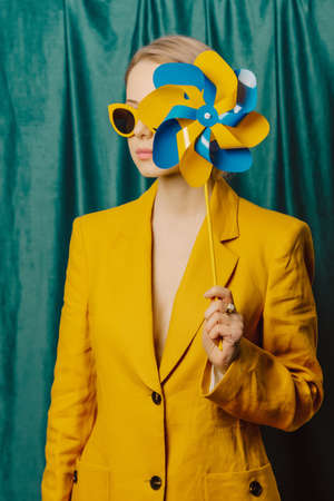 Stylish ukrainian woman in yellow sunglasses and jacket with pinwheel on green curtains backgroundの写真素材