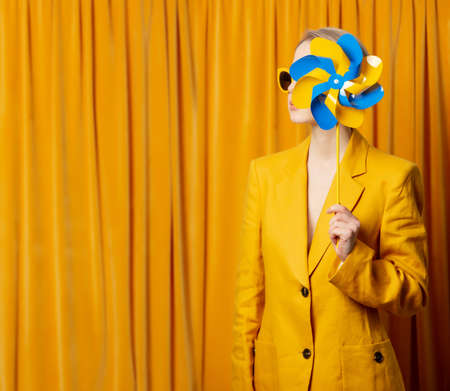 Stylish ukrainian woman in yellow sunglasses and jacket with pinwheel on curtains backgroundの写真素材