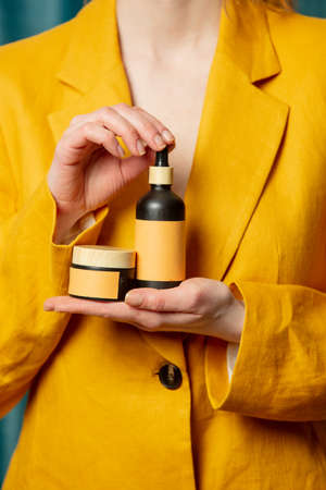 Stylish woman in yellow jacket hold cosmetic bottleの写真素材