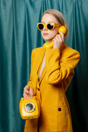 Stylish ukrainian woman in yellow sunglasses and jacket with deal phone on green curtains backgroundの写真素材