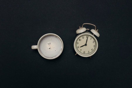 top view of a coffee cup and a vintage white alarm clock on a black background, creating a calm and nostalgic vibeの写真素材