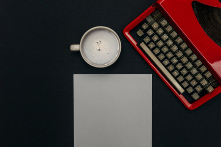 A top view of a coffee cup, white sheet of paper, and a vintage red typewriter on a black backgroundの写真素材