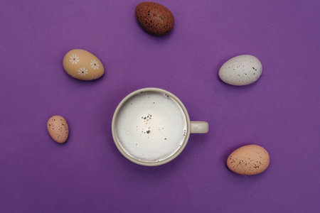 Decorative Easter eggs and a cup of coffee on a violet background, top view.の写真素材