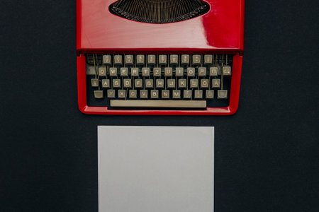 A top-down view of a vintage red typewriter, a white sheet of paper on a black backgroundの写真素材