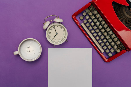 White alarm clock, coffee cup, red retro typewriter, and a white sheet of paper on a purple background, top view, concept of a writer or novel author.の写真素材