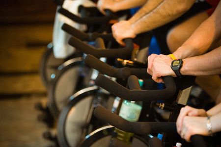 Active Lifestyle - Men & women pedalling on stationery bikes - Shallow DOF Focus on the hand with...