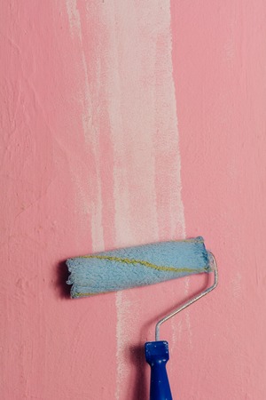 Paint roller leaning against the pink wall, with a white brushstroke on the rightの写真素材