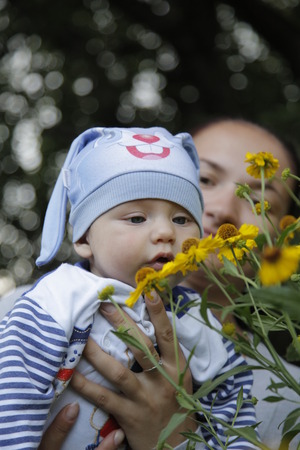 Baby in the hands of mom in the flower garden sniffing flowersの写真素材